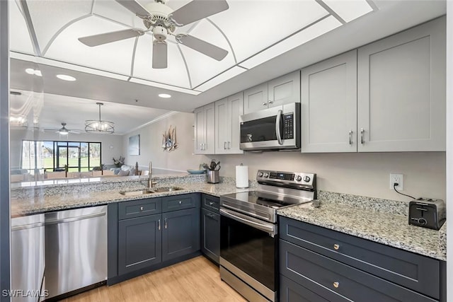 kitchen with light wood-style flooring, gray cabinets, a sink, appliances with stainless steel finishes, and light stone countertops