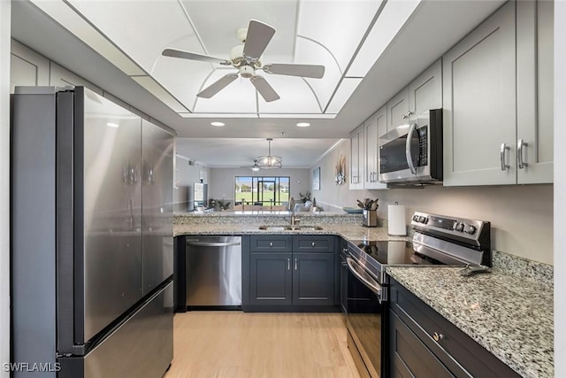 kitchen featuring light stone countertops, light wood-type flooring, a tray ceiling, appliances with stainless steel finishes, and a sink