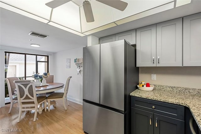 kitchen with visible vents, a ceiling fan, freestanding refrigerator, light wood-style floors, and light stone countertops