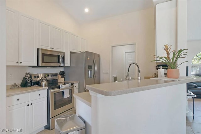 kitchen with stainless steel appliances, a kitchen bar, light countertops, and white cabinetry