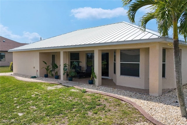 rear view of house with a yard, stucco siding, metal roof, and a standing seam roof