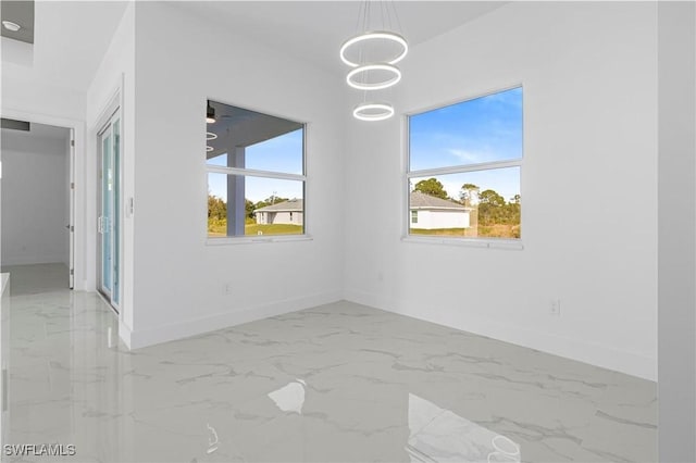 empty room featuring a chandelier, marble finish floor, a wealth of natural light, and baseboards