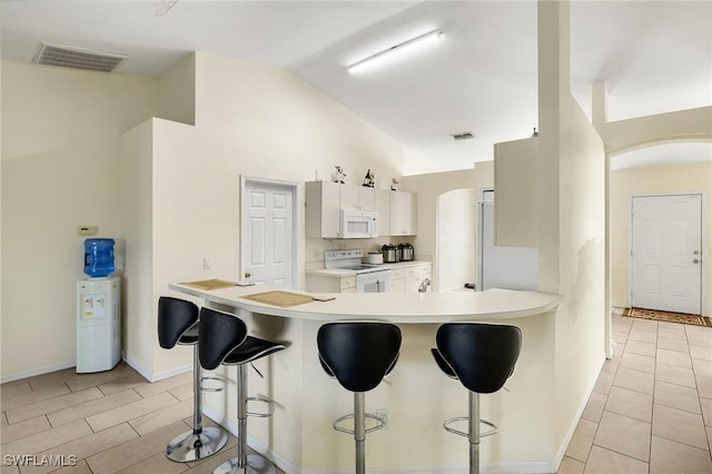 kitchen featuring white appliances, visible vents, a breakfast bar area, and white cabinetry