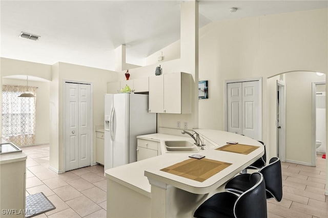 kitchen featuring arched walkways, white refrigerator with ice dispenser, visible vents, a sink, and a peninsula