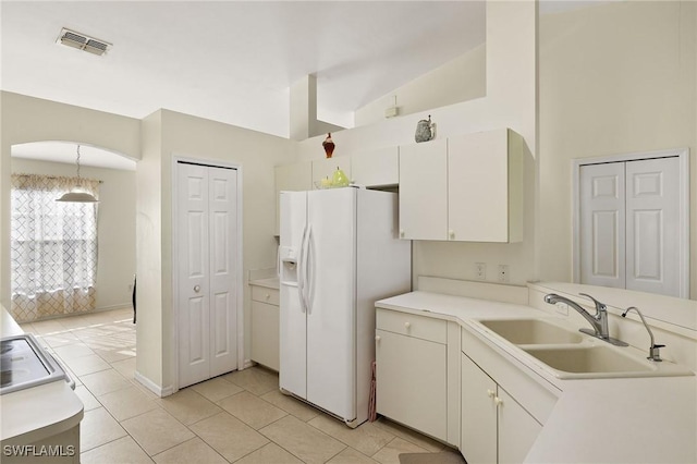 kitchen featuring light countertops, white refrigerator with ice dispenser, a sink, and visible vents