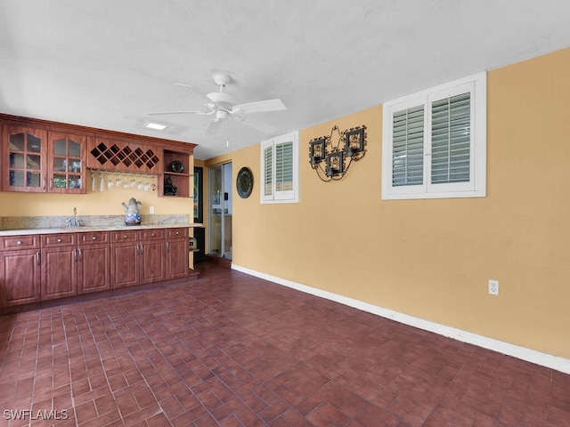 kitchen with light countertops, glass insert cabinets, ceiling fan, a sink, and baseboards