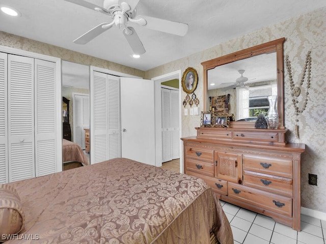 bedroom featuring wallpapered walls, baseboards, a ceiling fan, two closets, and light tile patterned flooring