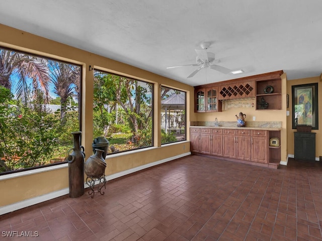 kitchen featuring baseboards, a ceiling fan, brick floor, open shelves, and a sink