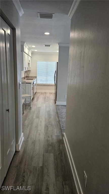 corridor with dark wood-style floors, baseboards, visible vents, a sink, and ornamental molding