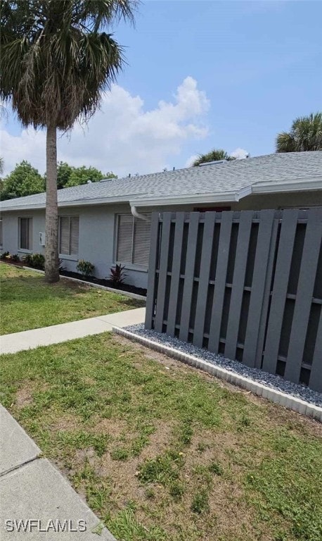 exterior space featuring a yard, roof with shingles, and stucco siding