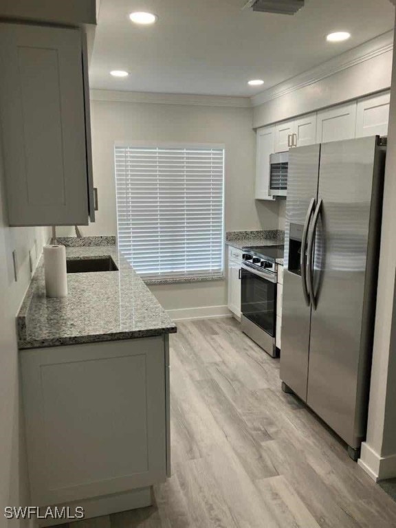 kitchen featuring light stone counters, stainless steel appliances, light wood-style floors, and ornamental molding