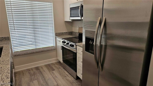 kitchen with light wood-style flooring, appliances with stainless steel finishes, white cabinets, baseboards, and light stone countertops