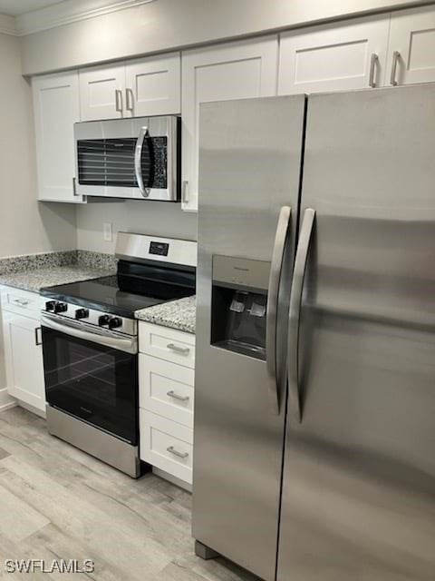 kitchen featuring light wood-style flooring, light stone counters, white cabinetry, appliances with stainless steel finishes, and crown molding