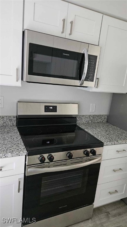 kitchen featuring white cabinets, appliances with stainless steel finishes, wood finished floors, and light stone countertops