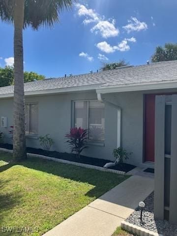 view of side of home with stucco siding, a lawn, and roof with shingles