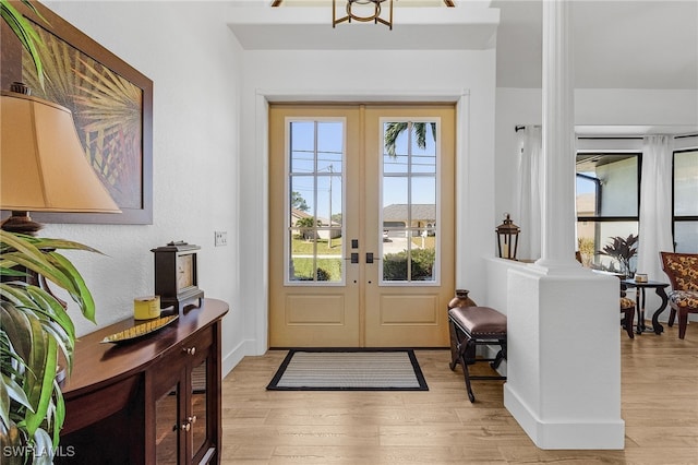 entrance foyer featuring ornate columns, light wood-style flooring, french doors, and baseboards