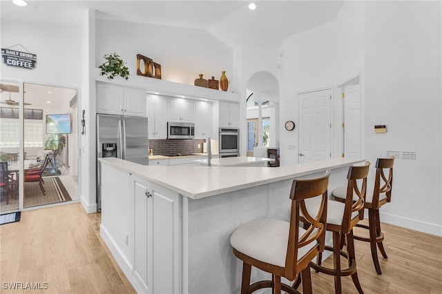 kitchen featuring light wood-type flooring, white cabinetry, stainless steel appliances, arched walkways, and decorative backsplash