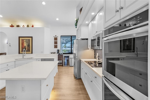 kitchen with a sink, a kitchen island, white cabinetry, appliances with stainless steel finishes, and light countertops