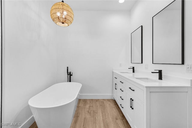 bathroom featuring wood finished floors, a freestanding bath, baseboards, and a sink