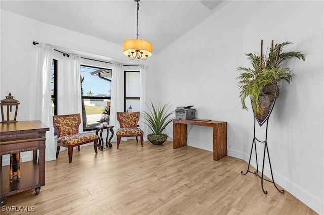 living area featuring visible vents, a notable chandelier, lofted ceiling, light wood finished floors, and baseboards