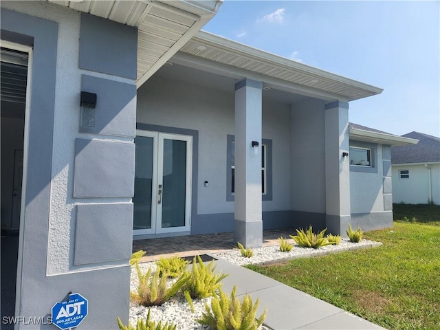 entrance to property featuring stucco siding, french doors, and a lawn