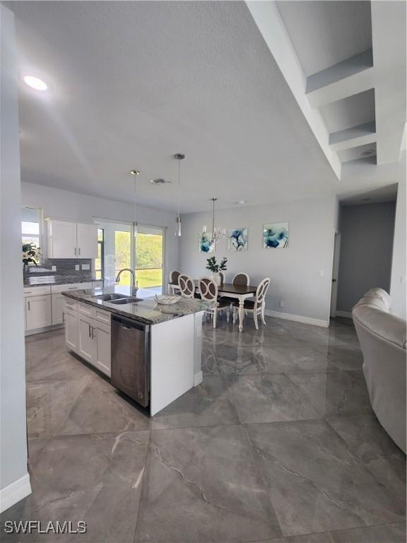 kitchen with baseboards, an island with sink, white cabinets, pendant lighting, and dishwasher