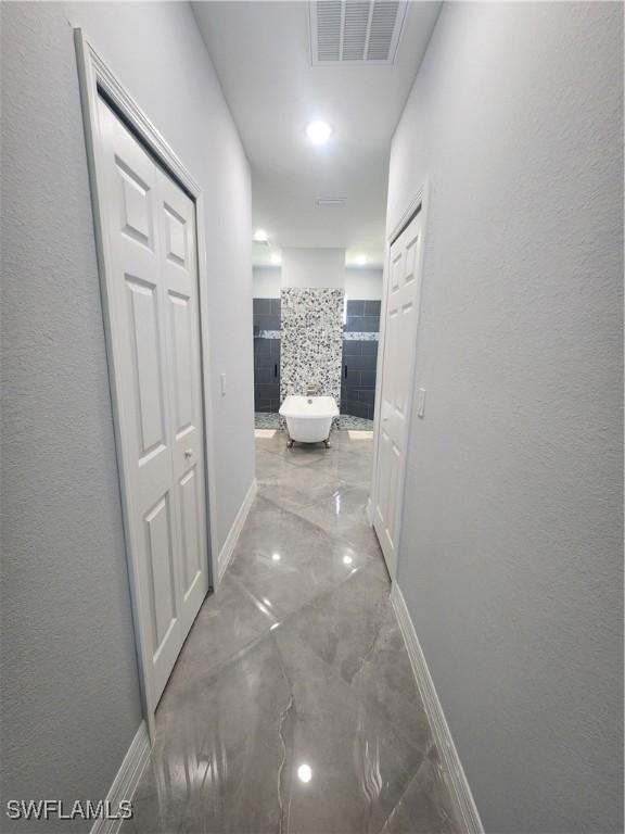 corridor featuring marble finish floor, baseboards, visible vents, and a textured wall