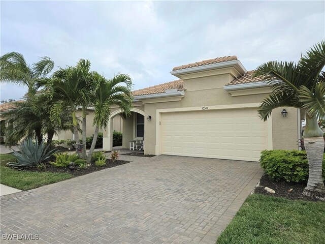 mediterranean / spanish-style house featuring stucco siding, a tile roof, decorative driveway, and a garage