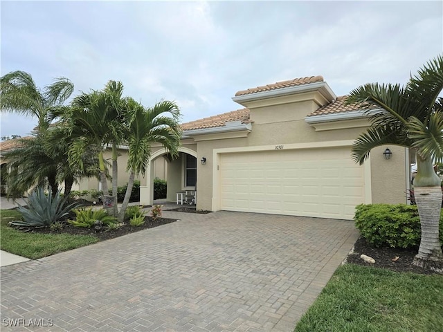 mediterranean / spanish-style house featuring stucco siding, decorative driveway, an attached garage, and a tiled roof