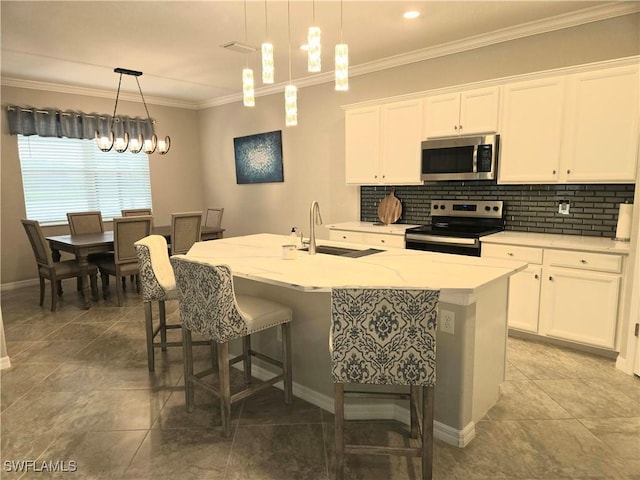 kitchen with a kitchen island with sink, ornamental molding, white cabinets, appliances with stainless steel finishes, and backsplash