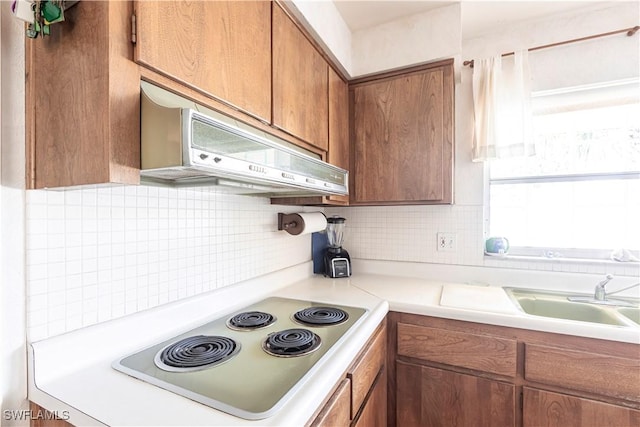 kitchen with brown cabinetry, extractor fan, electric stovetop, light countertops, and backsplash