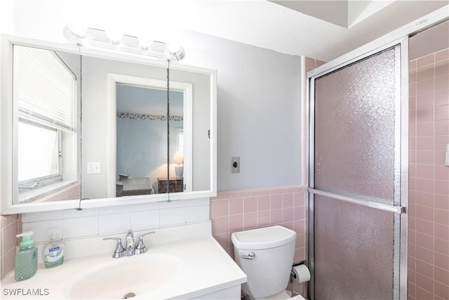 bathroom with a wainscoted wall, toilet, tile walls, a shower stall, and vanity