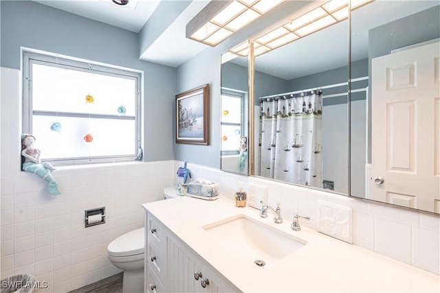 bathroom featuring toilet, a shower with shower curtain, tile walls, wainscoting, and vanity