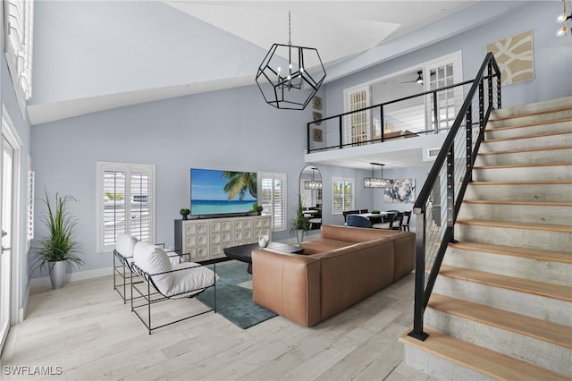 living area with baseboards, stairway, an inviting chandelier, wood finished floors, and high vaulted ceiling