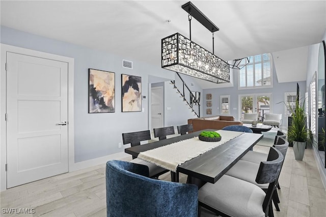 dining space featuring baseboards, visible vents, light wood-style flooring, stairs, and a towering ceiling