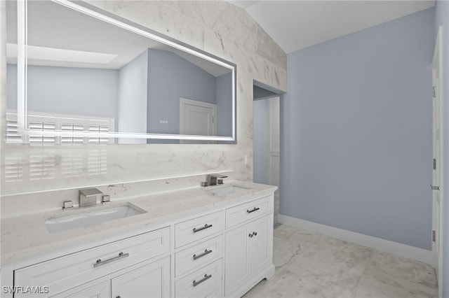 full bathroom featuring vaulted ceiling, double vanity, baseboards, and a sink