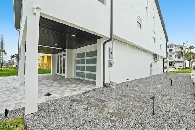 back of house featuring stucco siding, decorative driveway, a garage, and fence