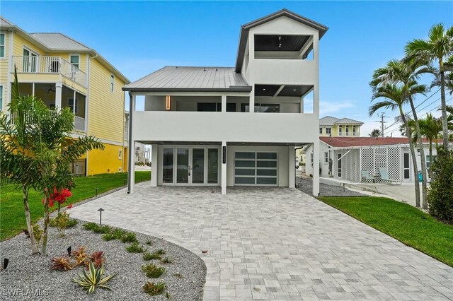 back of property featuring a balcony, stucco siding, french doors, a garage, and decorative driveway