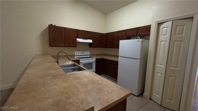 kitchen featuring electric range oven, freestanding refrigerator, a high ceiling, under cabinet range hood, and a sink