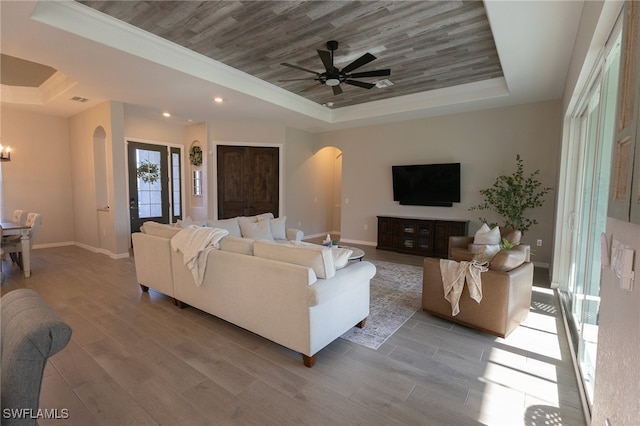 living room with a tray ceiling, arched walkways, baseboards, and wood finished floors