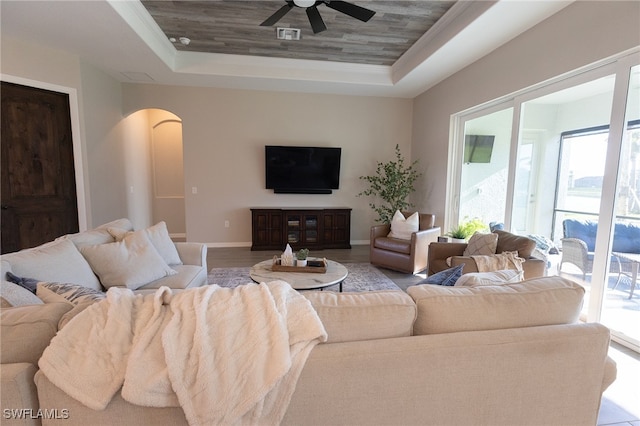 living room with baseboards, wood finished floors, arched walkways, a raised ceiling, and a ceiling fan