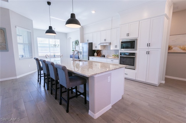 kitchen featuring an island with sink, under cabinet range hood, backsplash, white cabinetry, and appliances with stainless steel finishes