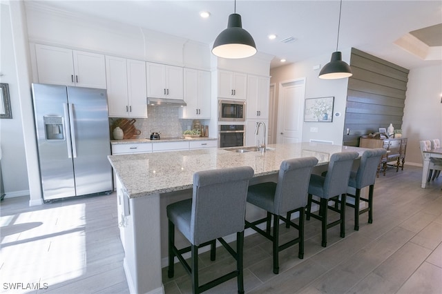 kitchen featuring a sink, under cabinet range hood, appliances with stainless steel finishes, white cabinetry, and backsplash