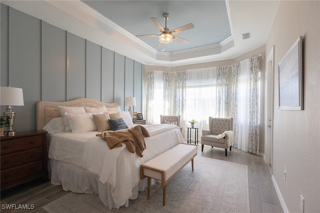 bedroom featuring baseboards, visible vents, light wood finished floors, a tray ceiling, and ornamental molding