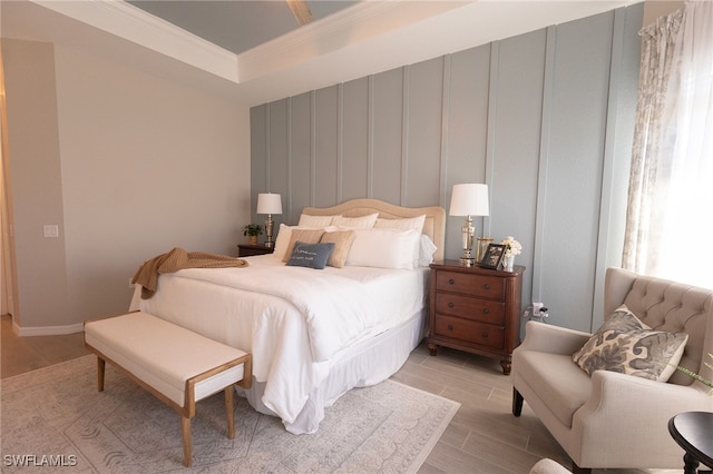 bedroom featuring wood finish floors, a tray ceiling, baseboards, and ornamental molding