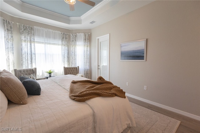 bedroom with visible vents, wood finished floors, baseboards, crown molding, and a raised ceiling