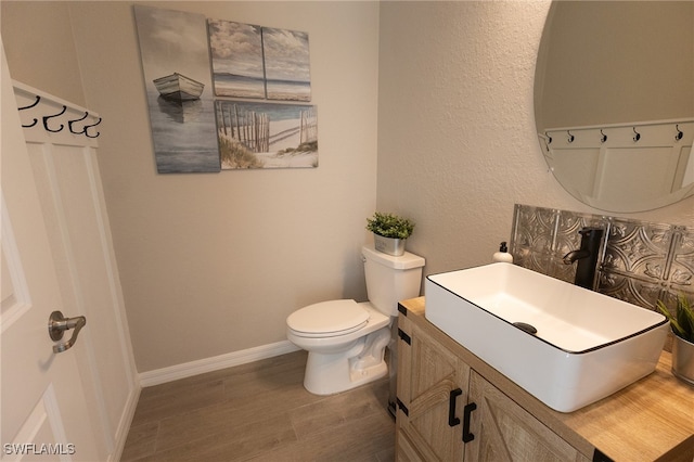 bathroom with toilet, vanity, baseboards, and wood finished floors