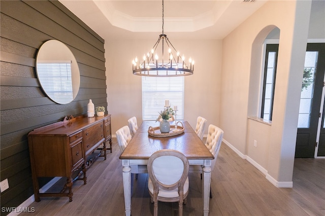 dining room with a raised ceiling, a notable chandelier, wood finished floors, and baseboards