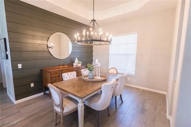 dining area with baseboards, wood walls, a tray ceiling, an inviting chandelier, and wood finished floors