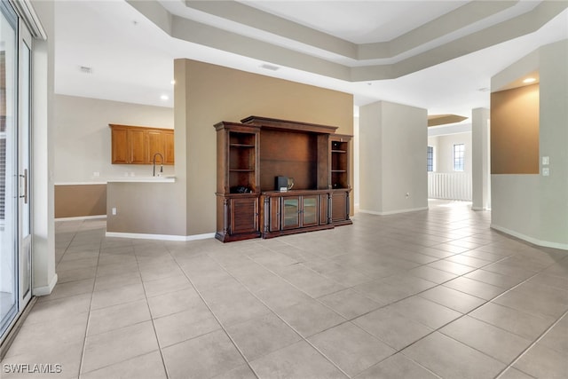 unfurnished living room with a sink, baseboards, and light tile patterned flooring